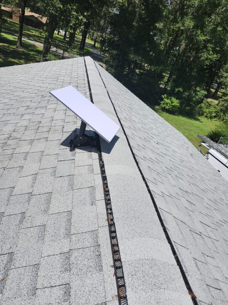 A Starlink Internet Antenna mounted to a roof. With a Outside cable run, down an outside wall, and a penetration through the wall that has a bushing and is siliconed.